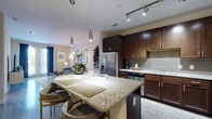 This single-story residence offers a thoughtfully designed open-concept layout that seamlessly connects the kitchen, dining, and living areas. The kitchen stands out as a central feature, showcasing rich dark-wood cabinetry, granite countertops, a mosaic tile backsplash, and a full suite of stainless steel appliances. A central island with seating provides both additional prep space and a casual dining option, while sleek pendant lights hang overhead and track lighting illuminates the work areas. Polished concrete flooring flows throughout the main living spaces, lending an upscale, contemporary feel.

The living area is comfortably proportioned, offering enough room for relaxed seating arrangements and accented by neutral walls that allow for flexible décor. The bedroom features plush carpeting, a ceiling fan, and windows that allow natural light and outdoor views, creating a calm and restful environment. A closet with wire shelving and a hanging rod provides practical storage. The bathroom is finished with a dark-wood vanity, polished countertops, and polished concrete flooring, maintaining the consistent modern aesthetic found throughout the residence. Overall, the space balances contemporary design elements with warm, inviting finishes.
