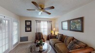 This single-story, one-bedroom, one-bathroom unit offers a thoughtfully organized layout across a comfortable footprint. The living room serves as the heart of the space, featuring a wood-burning fireplace, ceiling fan with light kit, carpet flooring, and multiple windows with blinds and draped curtains that allow for natural light control. Sliding glass doors provide direct outdoor access, enhancing the room's openness. Adjacent to the living area, a defined dining space accommodates a round table and chairs beneath a classic chandelier, with a large window and a built-in shelf niche adding character.

The galley-style kitchen is efficiently designed with ample upper and lower cabinetry, a double sink, dishwasher, electric range, refrigerator, and built-in microwave, all finished with light-toned countertops and tile flooring.

The bedroom is generously sized, offering plush carpet, a ceiling fan, textured ceiling, and windows with draping curtains. The full bathroom includes a tub-shower combination with a curtain rod and tile surround. Throughout the unit, textured ceilings and neutral wall tones create a cohesive, warm ambiance.