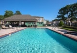 Located in Metairie, Louisiana, this single-story residence combines functional interior spaces with notable outdoor amenities. The exterior centerpiece is a generously sized rectangular swimming pool framed by brick-tiled coping and a spacious concrete deck, ideal for outdoor relaxation. A covered pergola with white columns connects the pool area to the structure, which features a low-pitched hip roof with warm-toned shingles.

Inside, the layout promotes an open flow between key living areas. A versatile room serves as a dedicated home office, featuring carpeted flooring, neutral painted walls, and ample space for a full desk setup and open shelving. This room connects directly to the living area, where hardwood-style flooring and a comfortable seating arrangement create a welcoming atmosphere. The kitchen is visible from the living space and includes cabinetry in a light finish alongside in-unit laundry.

The bedroom offers carpeted flooring, a reach-in closet, and a window with blinds providing natural light. Decorative touches throughout—including framed artwork, potted plants, and tasteful accents—contribute to a cohesive, well-maintained ambiance. The overall design prioritizes practicality and comfort throughout each connected space.
