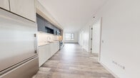 Located at 33 8th Street in San Francisco's SoMa neighborhood, this single-floor residence offers a thoughtfully designed contemporary interior with clean lines and a cohesive modern aesthetic throughout. Light wood-tone flooring flows continuously across the open-plan living area, creating a sense of warmth and visual continuity.

The kitchen is a standout feature, showcasing a sleek galley-style layout with light wood cabinetry at the base contrasted by dark charcoal gloss upper cabinets. Stainless steel Bosch appliances — including a range, microwave, and refrigerator — are integrated seamlessly, complemented by a white countertop and an undermount sink. Recessed lighting above the cabinetry provides focused illumination throughout the cooking area.

The kitchen opens directly into a bright, generously scaled living area that benefits from large windows, inviting substantial natural light and framing views of the surrounding urban cityscape. Additional rooms offer the same wood flooring and large windows with city views, providing a consistently bright and airy feel.

The bathroom is finished with marble-tiled walls in the tub and shower enclosure fitted with glass sliding doors, a floating wood vanity with a dark countertop and undermount sink, built-in open shelving, and large-format tile flooring — combining clean functionality with refined materials throughout.