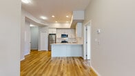This well-designed 2-bedroom, 2-bathroom unit is situated within a contemporary multi-story building and offers a thoughtfully efficient layout across a single floor. Light hardwood flooring flows consistently throughout the space, contributing to a clean, cohesive aesthetic.

The open-concept kitchen and living area serves as the heart of the unit. The kitchen features crisp white cabinetry extending to the ceiling, stainless steel appliances including a refrigerator, electric range, and built-in microwave, complemented by a white subway tile backsplash and light quartz countertops. A peninsula provides additional prep space and casual seating, opening seamlessly to the living area, which benefits from recessed lighting and a tray ceiling detail.

Both bedrooms are comfortably sized, each featuring large windows that invite natural light and offer views of the surrounding neighborhood. The primary bedroom includes an ensuite bathroom equipped with a single-sink vanity, white cabinetry, and a shower-tub combination. A second bathroom mirrors this clean, functional design. A private balcony accessible from the unit provides outdoor space with views of the building's modern exterior and landscaped surroundings.