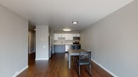 Located at 1709 Shattuck Ave in Berkeley, California, this single-floor unit offers a clean, modern aesthetic throughout. Rich dark hardwood flooring runs continuously across the space, providing a warm and cohesive foundation for each room.

The kitchen is thoughtfully designed with two-tone cabinetry — white upper cabinets paired with gray lower cabinets — and stainless steel appliances including a refrigerator, range, microwave, and dishwasher. A dining area adjacent to the kitchen provides a practical space for meals.

A well-proportioned hallway connects the main living areas to the private spaces, with natural light filtering in from a balcony at one end. The balcony offers views of the surrounding Berkeley neighborhood.

The bedroom is a comfortable, light-filled room featuring a tall window that allows ample natural light and frames views of the neighboring buildings and outdoor spaces. The room includes a desk and dresser, making it functional for both rest and work.

The bathroom is finished with consistent hardwood-style flooring, a glass-enclosed shower/tub combination, and a vanity with storage. The neutral gray tones carried throughout the unit lend the space a calm, contemporary character well-suited to its vibrant North Berkeley location.