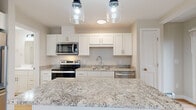 Located at 28 Hackamore in Scarborough, Maine, this single-floor residence offers a clean, modern aesthetic throughout. The kitchen serves as a central highlight, showcasing crisp white shaker cabinetry, striking granite countertops with sweeping natural veining, and a full suite of stainless steel appliances including a range, microwave, and dishwasher. A generous island with matching granite provides additional prep and seating space, while stylish pendant lights overhead add a contemporary touch. Light hardwood flooring runs through the kitchen and main living areas, creating a warm, cohesive feel. The bathroom features a white vanity with an integrated sink, clean lines, and a bright, neutral palette. The living spaces are finished in soft, neutral tones with generous natural light streaming in through well-placed windows, some offering views of the surrounding greenery. Bedrooms are carpeted for comfort and include baseboard heating, with one room also equipped with a wall-mounted mini-split unit for added climate control. A glass-panel exterior door in one of the rooms provides direct outdoor access and additional natural light. The overall design is bright, functional, and move-in ready, reflecting thoughtful finishes throughout.