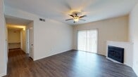 This single-story space is thoughtfully laid out, offering a functional and comfortable living environment. The main living area is expansive and open, featuring rich, dark hardwood-style flooring that extends throughout the common spaces. A ceiling fan with a light fixture provides both ventilation and ambient lighting, while a fireplace serves as a focal point along one wall. A sliding glass door fitted with vertical blinds allows natural light to fill the room and provides outdoor access.

Adjacent to the living area, a kitchen features a raised bar-style counter, white cabinetry, and standard appliances, creating a convenient pass-through layout that connects seamlessly to the rest of the space. A pendant light overhead adds a finishing touch to the area.

The bedrooms are carpeted in a neutral tone, offering a softer feel underfoot. Each room includes a ceiling fan, six-panel doors, and access to closet storage. The bathroom is well-appointed with a combined tub and shower enclosed by a curved curtain rod, white tile surround, a single-sink vanity, and hardwood-style flooring that ties into the overall aesthetic of the home.