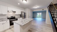 This two-story, 2-bedroom, 1-bathroom home offers a well-designed layout spread evenly across two floors, delivering a practical and comfortable living experience. The main floor opens to a bright, renovated kitchen that serves as a standout centerpiece, featuring crisp white shaker cabinetry, striking granite countertops with bold veining, a central island, stainless steel appliances including a refrigerator, electric range with hood, and dishwasher, all set atop light-toned hardwood-style flooring. The kitchen flows naturally into the living room, which benefits from a sliding glass door that invites natural light and provides outdoor views. The upper floor houses both bedrooms, each finished with the same light hardwood-style flooring and neutral warm-toned walls. The spacious primary bedroom features vaulted ceilings and a large window overlooking a wooded backdrop, while also offering dual closets for ample storage. The second bedroom is equally well-appointed with a closet and natural light. The shared full bathroom is cleanly finished in white, featuring a tub-shower combo, white vanity cabinetry, and matte black fixtures that add a modern contrast. A connecting hallway ties the upper level together efficiently.