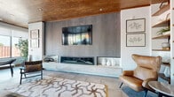 Located at 1414 Broadview Ave in Columbus, Ohio, this single-floor space delivers a refined, contemporary aesthetic through a thoughtfully curated blend of materials and design elements. Warm wood plank ceilings run throughout, providing an organic counterpoint to the otherwise modern palette and contributing to a welcoming, upscale ambiance.

The open layout is anchored by a striking feature wall clad in gray stone-effect panels, housing a wide linear fireplace beneath a wall-mounted display. A floating white stone hearth shelf adds a clean, minimalist accent, while large-format light gray tile flooring extends seamlessly across the entire space, enhancing the sense of openness.

The kitchen area commands attention with a dramatic black marble island featuring bold white veining, complemented by pendant lighting and crisp white cabinetry. Exposed steel structural beams add an industrial layer to the otherwise refined interior.

Generous windows line the perimeter, flooding the space with natural light and offering views of the surrounding neighborhood. Multiple seating arrangements—including lounge chairs, a sofa grouping, and bar-height seating—create distinct zones suited for both social gatherings and relaxed conversation. Lush indoor greenery and curated artwork complete the polished, inviting atmosphere.