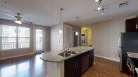 Located at 501 Willard St in Durham, NC, this single-floor residence offers a well-designed open-concept layout that seamlessly connects the kitchen, dining, and living areas. The kitchen is a standout feature, showcasing dark espresso cabinetry that extends to the ceiling for ample storage, granite countertops, and a full suite of stainless steel appliances including a refrigerator, electric range, and microwave. A curved kitchen island with a double basin sink and elegant pendant lighting serves as both a functional workspace and a natural gathering point. Warm hardwood-style flooring flows throughout the main living area, complemented by a ceiling fan and abundant natural light from a sliding glass door that opens to a private balcony. Neutral taupe-toned walls create a clean, cohesive aesthetic throughout the space. The bathroom is thoughtfully appointed with granite countertops on dark cabinetry, a large vanity mirror, tiled flooring, and a full tub-shower combination. Additional features include a spacious closet and track lighting accents. The overall ambiance is modern and inviting, combining practical design with upscale finishes in a comfortable, functional layout.
