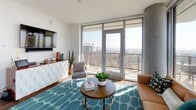 Located at 330 13th Street in San Diego, this high-rise model unit showcases contemporary urban living with an open, thoughtfully designed single-floor layout. The living area is anchored by expansive floor-to-ceiling windows and a glass-door balcony that frame sweeping panoramic views of the San Diego skyline and beyond, flooding the space with abundant natural light.

The kitchen is outfitted with warm wood cabinetry, a grey subway tile backsplash, stainless steel appliances including a gas range, microwave, dishwasher, and refrigerator, and a central island with bar seating — ideal for casual dining and entertaining. Rich hardwood-style flooring flows throughout the main living areas, adding warmth and continuity.

The unit features two well-appointed bedrooms, each benefiting from large windows with striking cityscape views. Both rooms include dedicated closet space and are accented by textured feature walls. Two bathrooms serve the unit — one with a full soaking tub and shower combination with clean white tile surround, and a second, more compact bathroom with tile flooring and a vanity. The overall design palette is clean and modern, combining white walls, natural wood tones, and contemporary fixtures to create a bright, cohesive living environment.