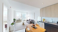 Located at 54 Jones Street in Jersey City, NJ, this well-appointed one-bedroom unit offers a thoughtfully designed open-concept layout across a single floor. The living room is bright and airy, featuring large floor-to-ceiling windows that frame sweeping views of the Jersey City skyline, flooding the space with abundant natural light. Light wood flooring runs throughout, complementing the clean, modern aesthetic.

The kitchen is outfitted with two-tone cabinetry—light wood uppers paired with navy lower cabinets—accented by a white subway tile backsplash and a full suite of stainless steel appliances, including a range, microwave, dishwasher, and refrigerator. Generous counter space and ample storage make it highly functional.

The open dining area connects seamlessly to the kitchen and living room, creating a cohesive and social living environment. The bedroom is a comfortable, well-proportioned retreat with its own large window offering expansive city and skyline views, along with light wood flooring and a dedicated closet. Throughout, the unit maintains a crisp, contemporary palette of whites and neutrals, contributing to a clean, modern ambiance ideal for urban living.
