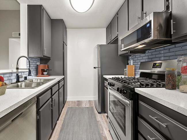 Blue tiled kitchen with stainless steel microwave, oven, and refrigerator. - Corbin Terrace