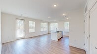 Located at 1010 Rosefinch Landing in Hoschton, Georgia, this single-story home offers a clean, contemporary design with an open-concept floor plan that maximizes both space and natural light. The main living and kitchen area is expansive and airy, with large windows fitted with blinds that allow abundant daylight to fill the room. Light-toned hardwood-style flooring flows throughout the main living spaces, enhancing the bright, modern aesthetic.

The kitchen is a standout feature, equipped with white shaker-style cabinetry extending to the ceiling for ample storage, granite countertops, and a full suite of stainless steel appliances including a refrigerator with ice maker, electric range, and built-in microwave. A central island with a granite surface and undermount sink provides additional prep space and serves as a natural gathering point.

The bedrooms are carpeted for comfort, offering a soft contrast to the hard flooring elsewhere. Generous closet space with wire shelving systems ensures practical storage. The bathroom is finished with consistent granite countertops, white cabinetry, a single undermount sink, and hardwood-style flooring. Multiple exterior doors provide convenient outdoor access. The overall interior palette of crisp whites and neutral tones creates a cohesive, move-in-ready environment.