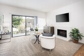 Located at 1104 Buckingham Dr in Costa Mesa, California, this single-story residence offers a thoughtfully designed layout with bright, neutral interiors throughout. The expansive living room is a standout feature, anchored by plush carpeting, a fireplace, and generous wall-to-wall sliding glass doors that flood the space with natural light and provide direct access to a private balcony overlooking lush greenery. A dedicated dining area sits adjacent to the main living space, highlighted by hardwood-style flooring and a large window with outdoor views. The kitchen is efficiently designed with white cabinetry, granite-style countertops, full appliance suite, and a distinctive recessed skylight ceiling that enhances brightness. The bedrooms are comfortably sized with soft carpeting and large windows framing peaceful outdoor views. The primary bedroom connects to a bathroom with dual vanity mirrors, granite-style countertops, and a spacious walk-in closet with built-in shelving. A full bathroom with a tub-shower combination, recessed lighting, and hardwood-style flooring serves the remaining rooms. Clean white walls and consistent finishes create a cohesive, airy ambiance throughout the entire residence.