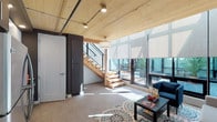 This two-story space at 2801 showcases a contemporary architectural design that blends natural materials with modern finishes throughout. The main level features an inviting living area with exposed wood plank ceilings, concrete floors, and a dramatic wall of floor-to-ceiling windows fitted with roller shades. These expansive windows frame views of a landscaped courtyard, flooding the interior with abundant natural light. A light wood open-riser staircase with black metal cable railings serves as a central design element, connecting the two levels with visual openness.

The kitchen is efficiently designed with dark and white two-tone cabinetry, a light-colored quartz countertop, a glass tile backsplash, and a full suite of stainless steel appliances including a refrigerator, range, microwave, and dishwasher. The bathroom on the main level features a dark wood vanity with a white undermount sink and a large mirror, while a full bathtub with shower is also present.

The upper level offers an airy, open loft-style layout with wide-plank light wood floors, crisp white walls, and generous natural light streaming through black-framed windows. This versatile upper floor provides an ideal flexible space for sleeping, working, or additional living needs.