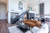 Located in the heart of downtown Salt Lake City on West Broadway, this sophisticated two-story residence offers a thoughtfully designed layout across two generous floors. The main level features an open-concept kitchen and living area anchored by a striking floor-to-ceiling tiled fireplace wall. The contemporary kitchen is outfitted with flat-front gray cabinetry reaching to the ceiling, stainless steel double wall ovens, a textured tile backsplash, a large island with quartz countertops, and open floating shelves — all complemented by warm hardwood flooring. A sleek cable-rail staircase connects the two levels. The hallway is lined with large-format windows that flood the space with natural light and offer city views. The primary bathroom is a standout, featuring marble-look tile floors, a glass-enclosed walk-in shower, a floating walnut vanity, and a large window overlooking the Salt Lake City skyline. The second bathroom echoes the modern aesthetic with warm wood cabinetry and a tub-shower combination. Both bedrooms are serene and well-proportioned, with plush carpeting and clean white walls. The upper-level primary bedroom features elegant pendant lighting. A walk-in closet with built-in shelving provides ample storage throughout.