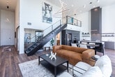 Located in the heart of downtown Salt Lake City on West Broadway, this sophisticated two-story residence offers a thoughtfully designed layout across two generous floors. The main level features an open-concept kitchen and living area anchored by a striking floor-to-ceiling tiled fireplace wall. The contemporary kitchen is outfitted with flat-front gray cabinetry reaching to the ceiling, stainless steel double wall ovens, a textured tile backsplash, a large island with quartz countertops, and open floating shelves — all complemented by warm hardwood flooring. A sleek cable-rail staircase connects the two levels. The hallway is lined with large-format windows that flood the space with natural light and offer city views. The primary bathroom is a standout, featuring marble-look tile floors, a glass-enclosed walk-in shower, a floating walnut vanity, and a large window overlooking the Salt Lake City skyline. The second bathroom echoes the modern aesthetic with warm wood cabinetry and a tub-shower combination. Both bedrooms are serene and well-proportioned, with plush carpeting and clean white walls. The upper-level primary bedroom features elegant pendant lighting. A walk-in closet with built-in shelving provides ample storage throughout.