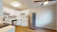 This single-floor unit features a clean, contemporary design with a neutral color palette and a mix of hard-surface and carpeted flooring throughout. The kitchen has been thoughtfully updated with crisp white shaker-style cabinetry accented by matte black hardware, white countertops, a light gray tile backsplash, and stainless steel appliances including a refrigerator and dishwasher. A ceiling fan is also present, adding practicality to the space. The living area is bright and open, featuring wood-look hard-surface flooring and a sliding glass door that provides direct outdoor access and views of surrounding greenery, filling the room with natural light. The bathroom is finished with a white vanity, white countertop, undermount sink, matte black faucet and hardware, a large mirror, and wood-look flooring. The bedrooms are carpeted for comfort, with textured ceilings, windows that invite natural light, and ample wall space. One bedroom includes a sliding mirrored closet door. Throughout the unit, clean white trim, neutral walls, and consistent finishes create a cohesive and move-in-ready atmosphere.