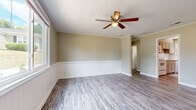 Located at 12 Georgetown Ct in North Augusta, SC, this single-story home efficiently arranges three bedrooms, one bathroom, a kitchen, and a hallway within a compact footprint. The layout, as revealed in the 3D model, positions rooms accessibly off a central hallway, maximizing the use of available space.

The spacious primary bedroom stands out as the largest room in the home, featuring gray-toned hardwood-style flooring, a ceiling fan with light fixture, white beadboard wainscoting along the lower walls, and crown molding. A large window allows ample natural light and outdoor views. The two secondary bedrooms are carpeted in neutral tones and each include a window for natural light and crown molding details.

The bathroom has been updated with a clean, modern aesthetic, showcasing shiplap accent walls, gray hardwood-style flooring, a full tub-shower combo, a white vanity, and a small window for ventilation. The hallway features the same hardwood-style flooring found throughout the common areas and connects all rooms efficiently. Throughout the home, warm beige wall tones, white trim, and consistent finishes create a cohesive, neutral palette.