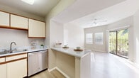 Located at 9801 N MacArthur Blvd in Irving, TX, this one-bedroom, two-bathroom residence offers a thoughtfully arranged single-floor layout that maximizes every square foot. Light wood-style flooring flows throughout, complementing the neutral warm-beige walls and crisp white trim that create a bright, cohesive aesthetic.

The combined kitchen and living area forms the heart of the home. The kitchen features cream cabinetry with wood-tone accents, granite-style countertops, a breakfast bar peninsula, and stainless steel appliances including a refrigerator and dishwasher. The adjoining living area benefits from elevated ceilings, a ceiling fan, and large windows alongside a sliding glass door that floods the space with natural light and opens directly onto the private patio.

The bedroom is a comfortable, sun-lit retreat with a window overlooking greenery, a ceiling fan, and ample closet access — three closets are distributed throughout the unit for generous storage. Both bathrooms are finished with granite-style vanity countertops, wood-tone cabinetry, and light flooring that carries the home's consistent design language. A patio provides outdoor space, rounding out this well-appointed Irving residence.