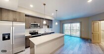Located in Naples, FL, this well-designed one-bedroom, one-bathroom residence offers a thoughtful, efficient layout across a single floor. The open-concept kitchen and living area serves as the heart of the home, featuring light wood-style flooring that flows seamlessly throughout. The kitchen is appointed with rich wood-tone cabinetry, a large center island with a crisp white countertop, stainless steel appliances including a French door refrigerator, range, microwave, and dishwasher, complemented by elegant pendant lighting overhead. A sliding glass door in the living area fills the space with natural light and provides direct access to a private balcony with outdoor views. The bedroom offers a calm, neutral palette with the same light wood flooring and a dedicated closet for storage. A louvered door leads to the in-unit laundry area, adding everyday convenience. The bathroom showcases a frameless glass walk-in shower with floor-to-ceiling white tile, a sleek vanity with an undermount sink, and marble-style tile flooring. Recessed lighting throughout enhances the bright, modern ambiance of this well-appointed Naples residence.