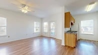 This single-floor residence offers a clean, functional layout designed to maximize comfort and usability throughout. The open living and dining area serves as the heart of the home, featuring warm wood-look laminate flooring that continues seamlessly throughout the space. Multiple windows along the exterior wall flood the room with natural light, while a ceiling fan overhead provides year-round comfort. A glass-paned door provides direct outdoor access, enhancing the sense of openness and connectivity to the exterior.

Adjacent to the living area, the galley-style kitchen is efficiently arranged with warm-toned wooden cabinetry lining both sides, offering generous upper and lower storage. Granite-patterned countertops provide durable workspace, and the kitchen is equipped with a full suite of white appliances including a range, dishwasher, and refrigerator. A window at the end of the kitchen brings in additional natural light.

The bedrooms are comfortably sized with neutral white walls, wood-look flooring, and individual windows. One bedroom benefits from a spacious walk-in closet outfitted with multi-tiered wire shelving for organized storage. The bathroom features a full soaking tub with white tile surround and brushed nickel grab bars, combining practicality with clean, classic styling.