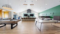 Located at 310 Northbend Drive in Charlotte, NC, this single-story amenity space is a thoughtfully designed community hub offering a diverse range of functional zones. The interior is characterized by soaring vaulted ceilings, light wood-look tile flooring, and a vibrant color palette of greens, teals, golds, and whites that energize the space throughout.

The central gathering area serves as the social heart of the space, anchored by a large U-shaped bar counter lined with contemporary upholstered barstools. Twin flat-screen TVs are mounted against a soft teal accent wall, and a coffee station and vending machines provide convenient refreshments. Dramatic pendant chandeliers with exposed Edison bulbs hang from the high ceiling, adding warmth and visual interest.

Adjacent to the lounge is a recreation area featuring a full-size pool table beneath a dome pendant light, alongside intimate booth-style seating with semi-private dividers — ideal for casual gatherings or focused work. A bright, welcoming corridor with bold green accent walls, abstract artwork, and yellow lounge seating connects the main zones seamlessly.

A dedicated conference room offers a more private setting, furnished with a long white table, ergonomic seating, floor-to-ceiling windows, and a wall-mounted display screen. A business services nook with printing capabilities and a private office space round out the functional offerings, making this a well-equipped and inviting community facility.