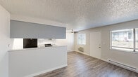 Located at 1204 E 30th Ave in Spokane, WA, this one-bedroom, one-bathroom unit offers a practical and efficient single-floor layout. The combined kitchen and living area serves as the heart of the home, featuring durable hardwood-style flooring, a textured ceiling, and a ceiling fan. Multiple windows with blinds fill the space with natural light, while a wall-mounted AC unit and baseboard heating ensure year-round comfort. The kitchen is equipped with gray cabinetry, light countertops, a black refrigerator, and a gas range, with a pass-through counter that opens to the living area. A hallway with a sliding-door closet connects the main living space to the private bedroom, which is carpeted and includes a window with outdoor views and a baseboard heater. The bedroom provides direct access to the full bathroom, which features an accessible roll-in shower with white subway tile, mosaic tile flooring, and stainless steel grab bars. A dedicated closet offers additional storage. The unit's clean, neutral palette throughout creates a bright and functional living environment.
