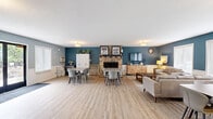 Located at 8848 Goodrich Rd in Bloomington, MN, this single-floor space offers an open-concept layout that seamlessly combines a living room and kitchen into one cohesive and functional area. The living room is defined by bold teal accent walls, light luxury vinyl plank flooring, and a striking stone fireplace that serves as a natural focal point. Large windows along multiple walls flood the space with natural light while offering pleasant outdoor views of the surrounding greenery. The seating area is generously proportioned, with ample room for multiple conversation groupings and dining arrangements.

The kitchen is thoughtfully designed with white shaker-style cabinetry, dark granite countertops, and a classic subway tile backsplash. Stainless steel appliances, including a full-size refrigerator and electric range, provide a modern touch, while the peninsula with bar seating offers a convenient casual dining option. A pass-through window connects the kitchen visually to the living area, enhancing the open and airy feel of the space.

French doors lead to an exterior entry, further connecting the interior to the outdoors. The consistent light-toned flooring and cohesive blue-gray and teal color palette throughout create a calm, inviting ambiance that is both modern and welcoming.
