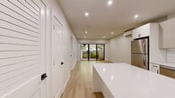 Located at 16 Congress St, Unit 102 in Beverly, MA, this thoughtfully designed one-bedroom, one-bathroom residence offers a clean, contemporary aesthetic across a single floor. Light hardwood flooring runs throughout the entire unit, creating a cohesive and airy feel.

The open-concept kitchen and living area serves as the heart of the home. The kitchen is outfitted with stainless steel appliances — including a gas range, over-the-range microwave, refrigerator, and dishwasher — complemented by light wood cabinetry, a white subway tile backsplash, and a central island with a white countertop that provides additional prep and dining space. Recessed lighting illuminates the area effectively. The living space adjoins the kitchen and features large sliding glass doors that open to an outdoor area, allowing natural light to pour in and offering views of the surroundings.

The bedroom is a well-proportioned private retreat featuring a wall-mounted mini-split HVAC unit for individual climate control and a double-door closet. The neutral palette and light flooring keep the room feeling bright and open.

The bathroom maintains the home's modern design language with a wall-mounted floating vanity, framed mirror, matte black fixtures and hardware, and continued light hardwood-style flooring. Clean white walls and bright vanity lighting complete the polished look.