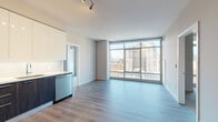 This single-floor residence showcases a contemporary design with clean lines and a neutral palette throughout. The open-plan living and kitchen area is anchored by a dramatic floor-to-ceiling window wall that frames sweeping urban skyline views, flooding the space with natural light and creating a strong visual connection to the city beyond.

The kitchen is well-equipped with a full suite of stainless steel appliances, including a side-by-side refrigerator, gas range, built-in microwave, and dishwasher. Cabinetry combines dark wood lower units with high-gloss white upper cabinets, complemented by a light subway tile backsplash and sleek countertops. Light wood-style flooring runs throughout the main living areas, reinforcing the modern aesthetic.

The bedroom offers carpeted flooring for added comfort and benefits from its own large window with city views. Two bathrooms serve the unit: one features a glass-enclosed walk-in shower with grey subway tile surround and polished chrome fixtures, while the second includes a soaking tub with tiled surround, a dark-cabinetry vanity with a white countertop, and light tile flooring. The overall ambiance is clean, contemporary, and urban.