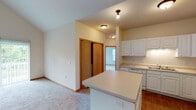 This single-floor residence offers a thoughtfully laid-out interior with a clean, neutral aesthetic throughout. The living area is a standout feature, boasting dramatic vaulted ceilings that create an expansive, airy atmosphere. A sliding glass door floods the space with natural light and provides direct access to the outdoors, where views of surrounding greenery are visible. Plush carpet flooring runs throughout the living and bedroom areas, complemented by warm wood-tone baseboards and trim.

The kitchen is well-appointed with ample white raised-panel cabinetry offering generous storage, light-toned countertops, a double-basin stainless steel sink, and white appliances including a range, refrigerator, and dishwasher. A kitchen island with additional counter space connects the kitchen to the adjacent carpeted dining or living area. Natural wood-finished sliding closet doors add warmth to the hallway and bedroom spaces.

The bedrooms are generously sized with large windows that invite natural light, and each includes built-in closet storage. Two full bathrooms serve the residence: one features a tub/shower combination, tile flooring, and a vanity with white cabinetry, while the second offers a wide vanity with a large mirror and chrome fixtures. The overall design is practical, bright, and move-in ready.