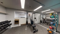 Located at 1029 Des Plaines Ave in Forest Park, Illinois, this single-floor fitness facility is thoughtfully organized into distinct workout zones designed to support a full range of exercise routines. The space features durable rubber flooring throughout, providing both safety and comfort underfoot.

The primary strength training area is finished with neutral gray walls and illuminated by bright overhead fluorescent lighting. A Body-Solid cable machine and adjustable weight bench serve as the centerpiece, complemented by a full rack of dumbbells for free-weight training. A large floor-to-ceiling mirror along one wall visually expands the space while allowing users to monitor their form. Glass block windows along the upper wall allow diffused natural light to filter in, adding to the functional atmosphere. A wall-mounted heater ensures year-round comfort.

A separate cardio room, distinguished by bold teal-painted walls, houses a treadmill and a stationary bike positioned near glass block windows. This vibrant, energizing space also includes a wall-mounted air conditioning unit for climate control during intense sessions.

Entry to the facility is through a frosted glass door with aluminum framing, offering a clean, professional aesthetic. Overall, the space presents a practical and well-maintained environment suitable for focused personal training or general fitness use.