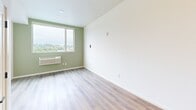 Located on the fifth floor at 120 Olympia Ave NE in Olympia, Washington, this single-floor unit combines contemporary design with functional efficiency. Light wood-style flooring runs throughout, creating a cohesive and easy-to-maintain foundation across all spaces.

The main living area is a standout feature, anchored by a bold sage green accent wall and a large picture window that frames elevated views of the surrounding treetops and neighborhood rooftops. A wall-mounted HVAC unit provides climate control directly beneath the window, and the open layout offers flexibility for a variety of furniture arrangements.

The kitchen is thoughtfully outfitted with white shaker-style cabinetry, dark countertops, a stainless steel range, a full-size refrigerator, and a compact countertop dishwasher. A stainless steel sink and under-cabinet storage add practicality to the space.

The bathroom maintains the unit's clean aesthetic with white cabinetry, a dark countertop vanity, a large mirror, and chrome fixtures, all set against neutral walls and the same wood-style flooring.

The entry corridor includes a built-in mailbox or panel, providing a convenient and organized welcome into the unit. Throughout the space, white walls, consistent flooring, and natural light from elevated windows contribute to a bright, modern ambiance.