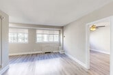Located in the Chevy Chase neighborhood of Washington, DC, this one-bedroom, one-bathroom residence offers a thoughtfully designed layout across a single floor. Light-toned hardwood-style flooring runs throughout the living areas, complementing the neutral beige walls and clean white trim that define the interior aesthetic.

The combined dining and living area is bright and open, featuring multiple windows dressed with blinds that allow generous natural light to fill the space. A radiator unit beneath the windows provides efficient heating, and the open sightline into the bedroom creates a sense of expansiveness.

The bedroom is a comfortable, well-proportioned retreat equipped with a ceiling fan and light fixture, a window overlooking the surrounding area, and a radiator. A closet provides convenient built-in storage.

The kitchen is efficiently designed with white shaker-style cabinetry, quartz countertops, a stainless steel sink, and a full suite of stainless steel appliances including a gas range, microwave, and refrigerator. Marble-look tile flooring adds a polished finish.

The bathroom continues the refined aesthetic with floor-to-ceiling marble-style tile, a glass-enclosed shower, and brushed nickel fixtures. An entry area with a closet and front door with gold hardware completes the floorplan of this well-appointed Washington, DC residence.