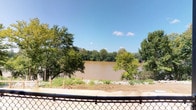 This single-story space is defined most prominently by its exceptional outdoor setting and natural surroundings. The standout feature is an expansive riverfront view, where a wide, flowing river stretches across the horizon, flanked by dense tree lines on the opposite bank. The scene is open and picturesque, with mature trees framing the view on either side and a clear blue sky overhead that enhances the sense of openness and natural light. A chain-link fence marks the perimeter boundary, offering an unobstructed sightline to the water and the lush greenery beyond. The riverbank area includes freshly laid gravel and exposed earth, suggesting recently completed or ongoing landscaping work that aims to refine the connection between the built space and its natural environment. The overall ambiance of this space is one of tranquility and natural beauty, with the river serving as a constant, dynamic backdrop. The combination of the waterfront proximity, the mature surrounding vegetation, and the expansive sky creates an environment that feels both open and grounded in nature. Interior details are limited based on available imagery, but the setting strongly positions this as a space where the outdoor environment is a central and defining characteristic.