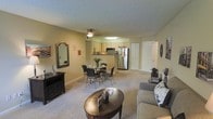 Located at 3400 S. Lowell Blvd. in Denver, Colorado, this single-floor residence offers a welcoming and functional open-concept layout that seamlessly connects the living, dining, and kitchen areas. The living room is generously sized, featuring plush carpeting in a neutral tone that extends throughout the common areas, creating a cohesive and comfortable atmosphere. A cozy seating arrangement anchors the space, complemented by a classic media console and decorative mirror that add character to the room. The dining area sits adjacent to the living space, accommodating a round table with elegant wrought-iron style chairs, ideal for everyday dining. The kitchen is efficiently designed with light wood cabinetry, a stainless steel refrigerator, and modern appliances, providing ample functionality. A breakfast bar serves as a natural divider between the kitchen and dining area, enhancing the open feel of the floor plan. Soft, ambient lighting fixtures illuminate the space, while a textured ceiling adds visual depth. A white paneled door leads to additional rooms, suggesting well-organized private quarters. The overall ambiance is warm, inviting, and move-in ready, making this Denver residence a practical and comfortable home.