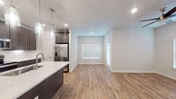 This single-floor unit showcases a thoughtfully designed open-concept layout with clean, modern finishes. The kitchen serves as a central highlight, featuring rich dark-stained shaker cabinetry extending to the ceiling, white quartz countertops, a full suite of stainless steel appliances including a French door refrigerator, electric range, and built-in microwave. A large center island with an undermount sink and elegant pendant lighting anchors the space, flowing seamlessly into the open living and dining area. Wood-look plank flooring runs throughout the main living spaces, adding warmth and continuity.

The bedrooms are well-proportioned, each outfitted with ceiling fans and natural light from window blinds. The primary suite connects directly to a dedicated bathroom featuring a lengthy white vanity with quartz countertops, backlit mirrors, large-format tile flooring, and access to a walk-in closet. A secondary full bathroom offers a soaking tub with tiled surround, white cabinetry, and matching quartz surfaces. Neutral grey-toned walls, recessed lighting, and crisp white trim unify the space, creating a bright and cohesive interior atmosphere throughout.