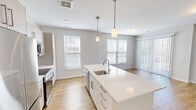 Located at 83 Pleasant Valley St in Methuen, MA, this four-bedroom, two-bathroom residence offers a well-designed single-floor layout with a clean, modern aesthetic throughout. The open-concept kitchen and living area serves as the heart of the home, featuring a large center island with an undermount sink, white shaker-style cabinetry, stainless steel appliances including a refrigerator, range, and microwave, and warm hardwood flooring. Pendant lighting above the island adds a refined touch to the space. The living area extends toward a sliding glass door that opens onto a private balcony, offering scenic outdoor views — an ideal spot for relaxing or entertaining. The four bedrooms are comfortably sized, with the primary bedroom providing a dedicated walk-in closet with built-in shelving. Bedrooms feature neutral carpet, large windows with blinds that allow ample natural light, and soft, neutral wall tones throughout. The two bathrooms are finished with white subway tile surrounds in the tub/shower combinations and chrome fixtures, offering a clean and timeless look. The overall design is bright, neutral, and move-in ready, creating a functional and comfortable living environment.