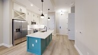 Unit 334, located in Decatur, GA, is a thoughtfully designed single-floor residence that makes efficient use of its space across four rooms. The kitchen serves as the centerpiece of the unit, showcasing floor-to-ceiling white shaker cabinetry, a striking teal island with a white quartz countertop and undermount sink, and a full suite of stainless steel appliances including a refrigerator, range, and built-in microwave. Stylish matte black pendant lights hang above the island, complementing the matte black hardware throughout. Light wood-look flooring ties the kitchen and entryway together seamlessly. The bedroom is a calm, neutral retreat featuring plush wall-to-wall carpet, a ceiling fan with integrated lighting, and a window with blinds that allows natural light to filter in. The bathroom is finished with elegant marble-look tile flooring, a white vanity with quartz countertop, an undermount sink, and a large black-framed mirror, all accented with matte black fixtures and hardware. The entryway is welcoming, featuring a classic paneled front door, recessed lighting, and a small chandelier that adds a refined touch. Overall, the unit presents a clean, modern aesthetic with cohesive design choices throughout.