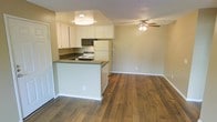 This single-floor residence offers a well-designed open-concept layout that seamlessly connects the kitchen and living area. Rich, warm-toned hardwood flooring runs throughout the main living space, adding a sense of warmth and cohesion to the interior.

The kitchen is positioned as a functional centerpiece, featuring a peninsula with a dark countertop that provides additional prep space and acts as a natural divider between the cooking and living zones. White cabinetry lines the upper walls, offering ample storage, while appliances include a built-in microwave, an electric range, and a full-size refrigerator. A recessed ceiling light fixture directly above the kitchen ensures well-lit meal preparation.

The adjacent living area is open and airy, finished with the same hardwood flooring and complemented by a ceiling fan with an integrated light fixture — a practical feature that aids in air circulation and ambient lighting. Neutral warm-beige walls provide a versatile backdrop throughout. White baseboards and trim add a clean, finished look to the space.

Textured ceilings are present throughout, adding a subtle architectural detail. The layout is efficient and functional, making strong use of the available floor space to create a comfortable, connected living environment.
