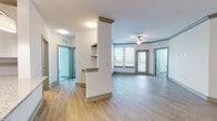 This thoughtfully designed single-floor residence offers a bright, open-concept layout that seamlessly connects the main living and kitchen areas. The spacious living room features light wood-look flooring, crown molding with a tray ceiling detail, a ceiling fan, and direct access to a balcony through glass-paneled doors that flood the space with natural light and provide outdoor views of lush greenery.

The kitchen is well-equipped with light-toned flat-panel cabinetry, granite countertops, stainless steel appliances including a refrigerator with ice maker, electric range, microwave, and dishwasher. A peninsula with pendant lighting and an undermount sink adds both style and functionality, while recessed lighting illuminates the space.

A partial wall with built-in shelving divides the kitchen from the entryway, which features a dedicated coat closet. The bedrooms are carpeted and offer generous natural light through large windows overlooking scenic outdoor landscapes, with ample closet storage including built-in wire shelving systems.

The residence includes two bathrooms: a primary bath with a double-sink granite vanity, wood-look flooring, and a tiled walk-in shower with a glass enclosure, and a secondary bath with a tiled tub-shower combination and granite vanity. The overall palette of whites, soft grays, and warm wood tones creates a clean, contemporary ambiance throughout.