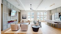 Located along South Blue Angel Parkway in Pensacola, Florida, this single-story clubhouse is designed as a contemporary community amenity space with a cohesive modern aesthetic throughout. Light hardwood flooring, neutral tones, and carefully selected furnishings create a polished yet approachable atmosphere across all areas.

The main lounge is a generously proportioned gathering space anchored by a coffered ceiling with a sleek ceiling fan and an expansive bank of tall windows overlooking the outdoor pool area, flooding the room with natural light. Comfortable seating arrangements, including plush sofas and swivel chairs, are organized around area rugs, encouraging relaxed socializing. A mounted television and built-in cabinetry accent one wall.

Adjacent to the lounge is a well-appointed kitchen and coffee bar area featuring gray cabinetry, white quartz countertops, a central island with upholstered gold-accented bar stools, and a stylish layered pendant light fixture overhead.

A dedicated conference and business center offers a round table with ergonomic seating, a workstation, and bold aviation-themed artwork beneath dramatic drum pendant lighting.

The fitness center is equipped with a full range of strength and cardio machines, rubber flooring, mirrored walls, and large windows providing natural light and views of the surrounding landscape.

A covered outdoor terrace connects seamlessly to the pool deck, furnished with modern lounge seating and large ceiling fans.