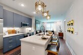 Located at 2408 South Blvd in Charlotte's vibrant South End neighborhood, this well-appointed one-bedroom, one-bathroom residence offers a thoughtfully designed open-concept layout across a single floor. The combined kitchen and living area serves as the heart of the home, showcasing bold slate-blue cabinetry with gold hardware, stainless steel appliances, a striking white quartz waterfall island with bar seating, and statement gold chandelier pendants that add a glamorous touch. Rich hardwood-style flooring and recessed lighting flow throughout the main living space, which connects seamlessly to a bright sitting area bathed in natural light from multiple windows. The living room features a sophisticated sage-green accent wall, creating a calm and curated atmosphere. The bedroom is carpeted for comfort and includes multiple windows, a ceiling fan, and a deep green accent wall that lends a bold, contemporary character. A dedicated closet provides organized storage. The bathroom is finished with marble-look tile flooring, clean white walls, and a glass-enclosed walk-in shower with sleek black hardware. A private balcony extends the living space outdoors, completing this polished and modern Charlotte residence.