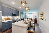 Located at 2408 South Blvd in Charlotte's vibrant South End neighborhood, this well-appointed one-bedroom, one-bathroom residence offers a thoughtfully designed open-concept layout across a single floor. The combined kitchen and living area serves as the heart of the home, showcasing bold slate-blue cabinetry with gold hardware, stainless steel appliances, a striking white quartz waterfall island with bar seating, and statement gold chandelier pendants that add a glamorous touch. Rich hardwood-style flooring and recessed lighting flow throughout the main living space, which connects seamlessly to a bright sitting area bathed in natural light from multiple windows. The living room features a sophisticated sage-green accent wall, creating a calm and curated atmosphere. The bedroom is carpeted for comfort and includes multiple windows, a ceiling fan, and a deep green accent wall that lends a bold, contemporary character. A dedicated closet provides organized storage. The bathroom is finished with marble-look tile flooring, clean white walls, and a glass-enclosed walk-in shower with sleek black hardware. A private balcony extends the living space outdoors, completing this polished and modern Charlotte residence.