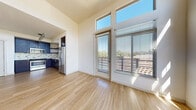 This thoughtfully designed single-floor residence combines contemporary style with everyday functionality. The open living area immediately impresses with its soaring ceiling height and expansive floor-to-ceiling windows paired with clerestory windows above, flooding the space with natural light and offering pleasant outdoor views of surrounding greenery. A glass door leads to a private balcony with horizontal wood-slatted railings, extending the living space outdoors. Light-toned hardwood flooring runs throughout the main areas, enhancing the bright, airy ambiance.

The kitchen is well-appointed with rich dark wood cabinetry, crisp white countertops, a decorative tile backsplash in neutral tones, and a full suite of stainless steel appliances including a gas range, built-in microwave, dishwasher, and French door refrigerator. Track lighting overhead adds a modern touch.

The bedrooms offer plush carpeting, generous closet storage with sliding doors, and large windows that invite natural light and views of the tree-lined surroundings. The bathroom is spaciously laid out with accessibility features including grab bars, a dark wood vanity with white countertop, a large mirror, and matching hardwood-style flooring. Overall, the unit presents a clean, modern aesthetic with quality finishes throughout.