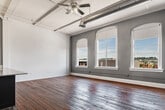 This generously sized two-bedroom, one-bathroom unit showcases a compelling blend of industrial and modern design elements throughout its single floor. Original wide-plank hardwood floors run throughout the space, displaying the rich character of aged wood that anchors the unit's loft-inspired aesthetic. Exposed ductwork and structural ceiling elements reinforce the industrial character, while elevated ceiling heights amplify the sense of openness.

The main living area is expansive and open, bathed in natural light from a row of arched windows that frame outdoor views. A cast-iron radiator near the windows adds a nod to the building's historic roots. The kitchen features a large peninsula with granite countertops, dark navy cabinetry, stainless steel appliances, and a chandelier overhead, seamlessly connecting to the living space.

Both bedrooms are well-proportioned with grey accent walls, ceiling fans, and hardwood floors. The primary bedroom offers generous space, while a dedicated closet adds practical storage. The hallways connect the rooms efficiently. The bathroom includes tile flooring, a full tub, a granite-topped vanity with dark cabinetry, and a large mirror.