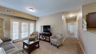 Located at 13350 S Greenwood St in Olathe, Kansas, this single-floor residence offers a thoughtfully designed open-concept layout that seamlessly connects the main living areas. The living room is warm and inviting, featuring plush carpeting, neutral wall tones, and French doors that invite natural light. It flows directly into the kitchen, which is outfitted with rich dark wood cabinetry, granite countertops, stainless steel appliances including a refrigerator, range, and microwave, and hardwood flooring. A breakfast bar peninsula bridges the kitchen and living space, making it ideal for casual dining or entertaining.

The primary bedroom is generously sized with soft carpeting and access to a walk-in closet. Its en-suite bathroom features hardwood flooring, a walk-in shower with grab bars, and a dark wood vanity with a clean white countertop. A second bedroom offers carpeted floors, a large window with outdoor views, and space for a daybed and desk, making it versatile as a guest room or home office. A secondary bathroom with hardwood flooring and a shower is also present. Throughout, the residence maintains a cohesive, neutral color palette that creates a calm and functional living environment.