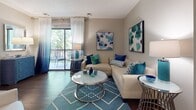 Located on Bywater Drive in Henrico, Virginia, this single-floor residence offers a thoughtfully designed layout with a cohesive teal and neutral color palette throughout. The living room serves as the centerpiece of the home, featuring hardwood-style flooring, large sliding glass doors that flood the space with natural light, and direct access to a private balcony overlooking lush, tree-lined surroundings — ideal for relaxing or outdoor dining.

The galley-style kitchen is equipped with dark espresso cabinetry, granite-look countertops, black appliances including a refrigerator and electric range, and a functional layout that maximizes efficiency. Adjacent to the kitchen is a dining area, completing a practical and connected living space.

The residence includes multiple bedrooms, each featuring plush carpeting, generous windows with views of greenery, and bold teal accent walls that add a distinctive design touch. The primary bedroom is particularly spacious, offering room for a full furniture suite.

The bathrooms are finished with dark wood vanities, white countertops, and hardwood-style flooring. A full bath includes a tub-shower combination with tiled surround, while an additional half bath provides added convenience for guests. Overall, the space balances comfort and style in a serene Henrico setting.