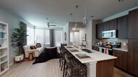 This single-floor residence showcases a thoughtfully designed open-concept layout that seamlessly connects the kitchen, dining, and living areas. The kitchen is a standout feature, equipped with dark espresso cabinetry extending to the ceiling, stainless steel appliances including a range, microwave, and refrigerator, and a tile backsplash. A generously sized island with a white quartz countertop, undermount sink, and seating for multiple guests serves as the centerpiece, illuminated by glass pendant lights overhead. Light hardwood flooring runs throughout the main living areas, complementing the neutral gray walls.

The living room benefits from corner windows dressed with horizontal blinds and floor-to-ceiling drapes, allowing abundant natural light while a ceiling fan adds comfort. An in-unit washer is tucked conveniently near the kitchen.

The bedrooms feature plush carpeting, large windows, and ceiling fans. The primary bedroom connects directly to a walk-in closet outfitted with multi-level shelving and hanging rods on all sides, providing ample storage. The en-suite bathroom offers a dual-sink vanity with dark wood cabinetry, quartz countertops, and a glass-enclosed tiled walk-in shower, completing this well-appointed residence.