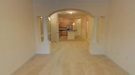 Located at 2792 Stantonsburg Rd in Greenville, NC, this single-floor property offers a thoughtfully designed open layout that emphasizes both style and functionality. A defining architectural feature of the space is the grand arched entryway flanked by decorative white columns, which elegantly frames the transition from the spacious living area into the kitchen and dining zone. The light-toned flooring throughout the main living area enhances the sense of openness and contributes to the bright, airy ambiance of the space. The kitchen is well-equipped, showcasing warm wood cabinetry, a stainless steel refrigerator, a central island with a dark countertop, and track lighting overhead that ensures ample illumination for meal preparation. Pendant lighting above the island adds a refined touch to the kitchen's overall aesthetic. The neutral color palette used throughout — from the soft wall tones to the light flooring — creates a cohesive and welcoming atmosphere. The open-concept design allows for a seamless flow between the living and kitchen areas, making the space ideal for both everyday living and entertaining. The combination of classic architectural details and practical modern finishes gives this property a distinctive and comfortable character.