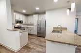 This 1,340-square-foot apartment at 3455 Kearny Villa Road, Unit 202, in San Diego, CA offers a thoughtfully designed single-floor layout with 3 bedrooms, 3 bathrooms, a combined kitchen and living area, a closet, and two hallways. Throughout the unit, durable wood-look flooring provides a cohesive, modern aesthetic. The kitchen is a standout feature, boasting white shaker-style cabinetry with black hardware, granite countertops, a central island with an undermount sink, and a full suite of stainless steel appliances including a gas range, microwave, and French door refrigerator. Track lighting and recessed fixtures illuminate the space effectively. The living area is open and bright, with clean white walls and ample room for flexible furniture arrangements. Each of the three bedrooms features wood-look flooring, white walls, and windows that invite natural light. The primary bedroom measures 160 square feet and includes a thermostat for individualized climate control. The three bathrooms are finished consistently, with wood-look flooring, white surrounds, and granite-topped vanities. Two bathrooms include shower-tub combos, while one features an accessible grab bar. Two hallways connect the spaces efficiently, completing this clean, functional San Diego apartment.